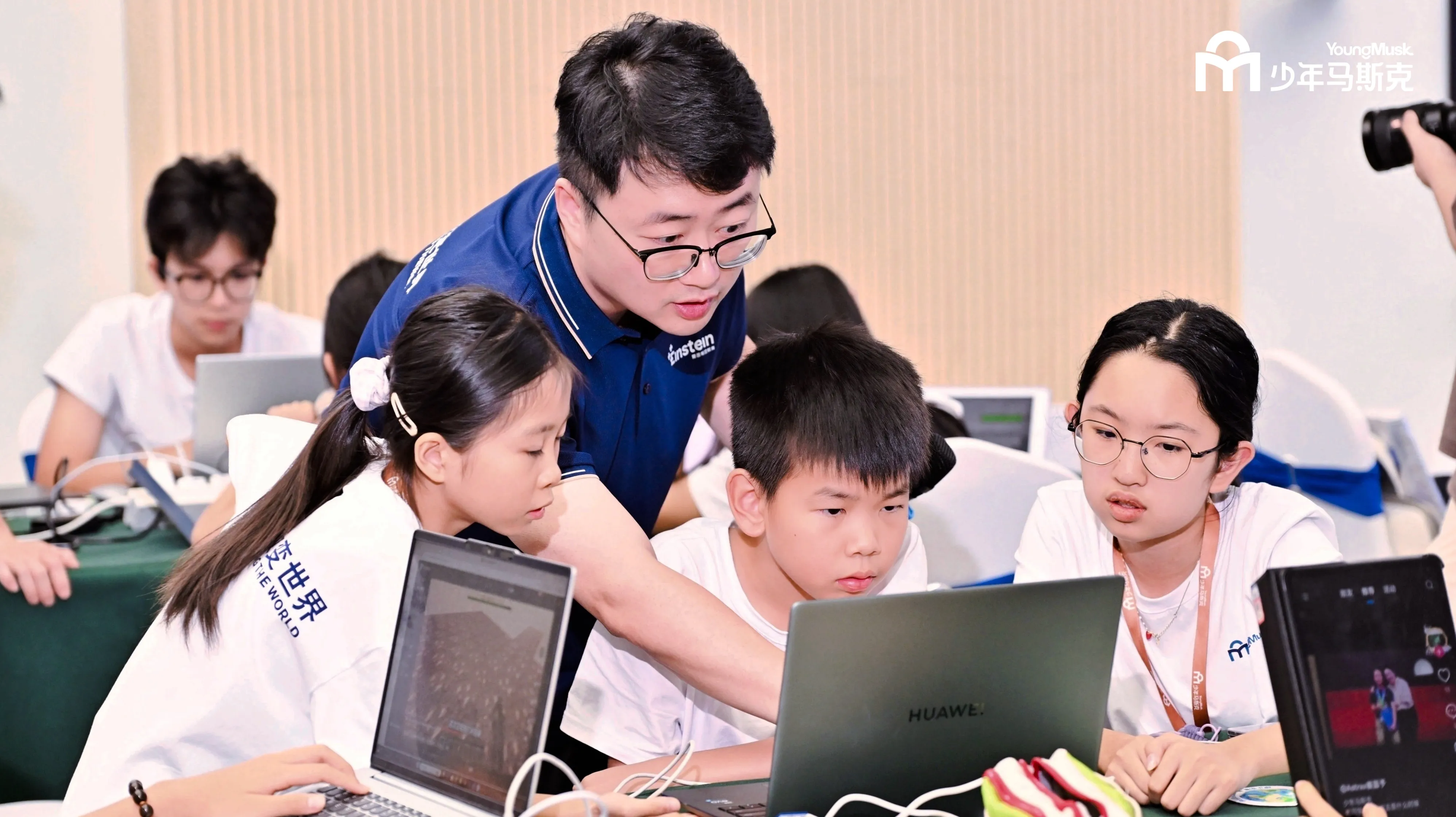 少年马斯克创业营现场，导师正在指导青少年团队使用电脑完成项目
